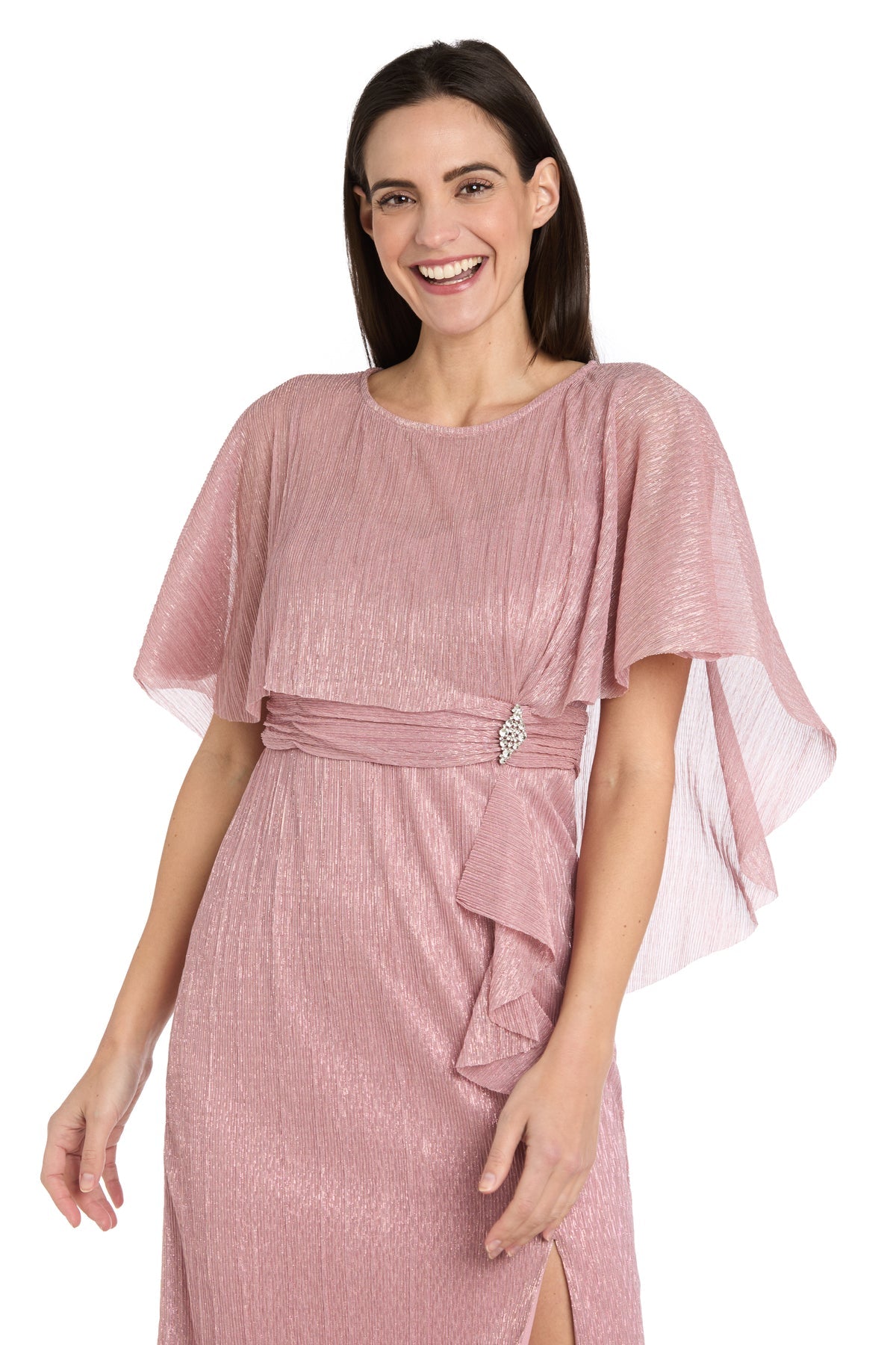 Smiling woman stands against a white background, wearing the R&M Richards 3195P Caped Knee-Length Party Dress—shimmery pink, petite fit, with short flutter sleeves, side sash detail, and brooch accent.